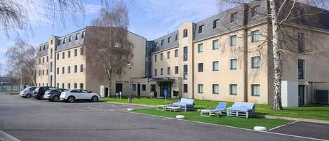 Un hôtel moderne à plusieurs étages, doté d’un parking et d’un espace extérieur aménagé pour s’asseoir.