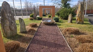 Un camino bordeado por piedras grandes y una fuente central, rodeado de arbustos y árboles cuidadosamente podados.