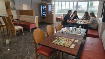 A restaurant with marble flooring, wooden chairs, and tables. There are people dining and a vending machine in the background.