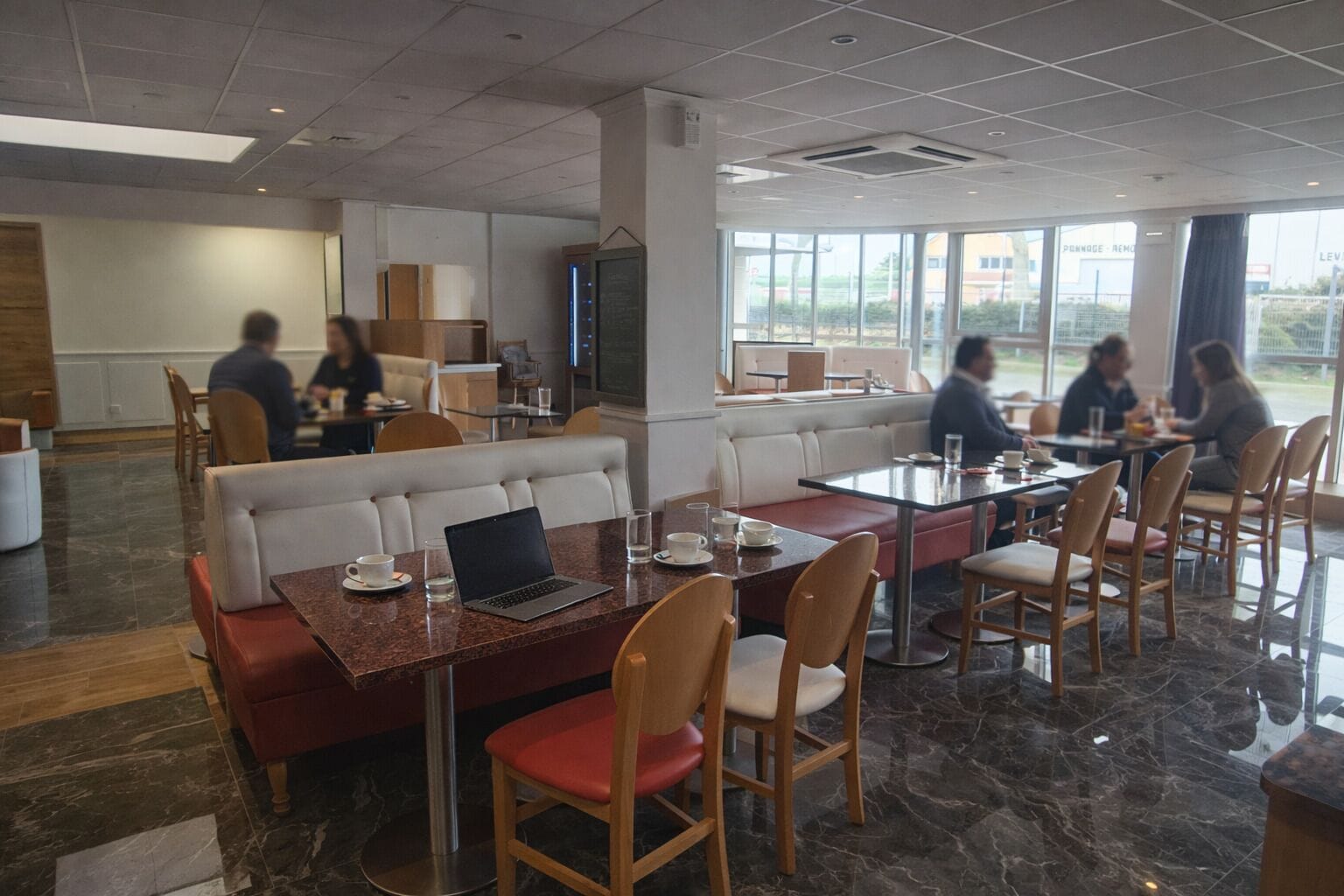 A modern dining area with booths and tables, large windows, and a view of the outside.