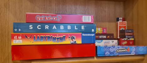 A shelf with various board games including Scrabble, Labyrinth, Ravensburger, and Qui Est-ce?.