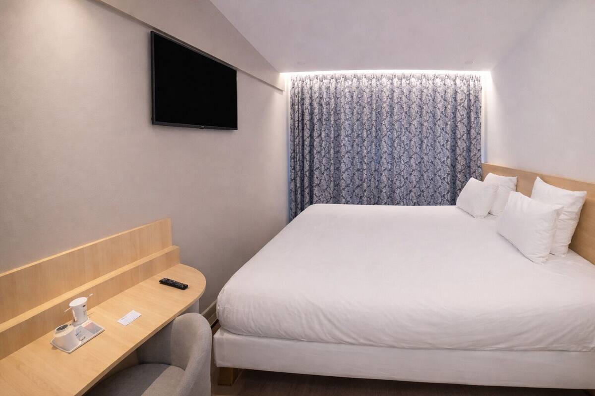 Ein Hotelzimmer mit Bett, Schreibtisch, Fernseher und Vorhang.