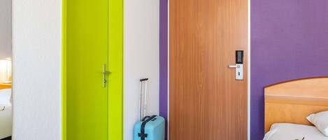 A hotel room with a bright green door, a wooden door, a bed with white bedding, and a suitcase on the floor.