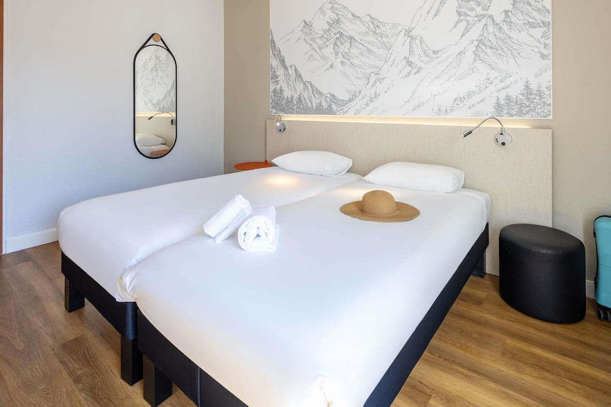 Una cama bien hecha con sábanas blancas, una toalla enrollada y un sombrero de paja sobre la cama.