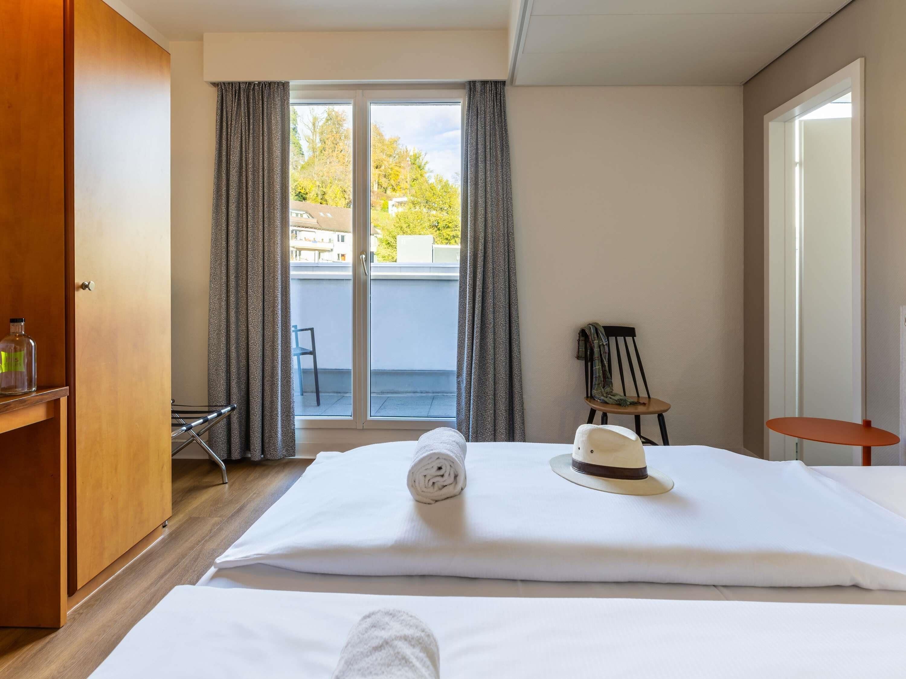 Een hotelkamer met een bed, een stoel, een klein tafeltje en een kast.