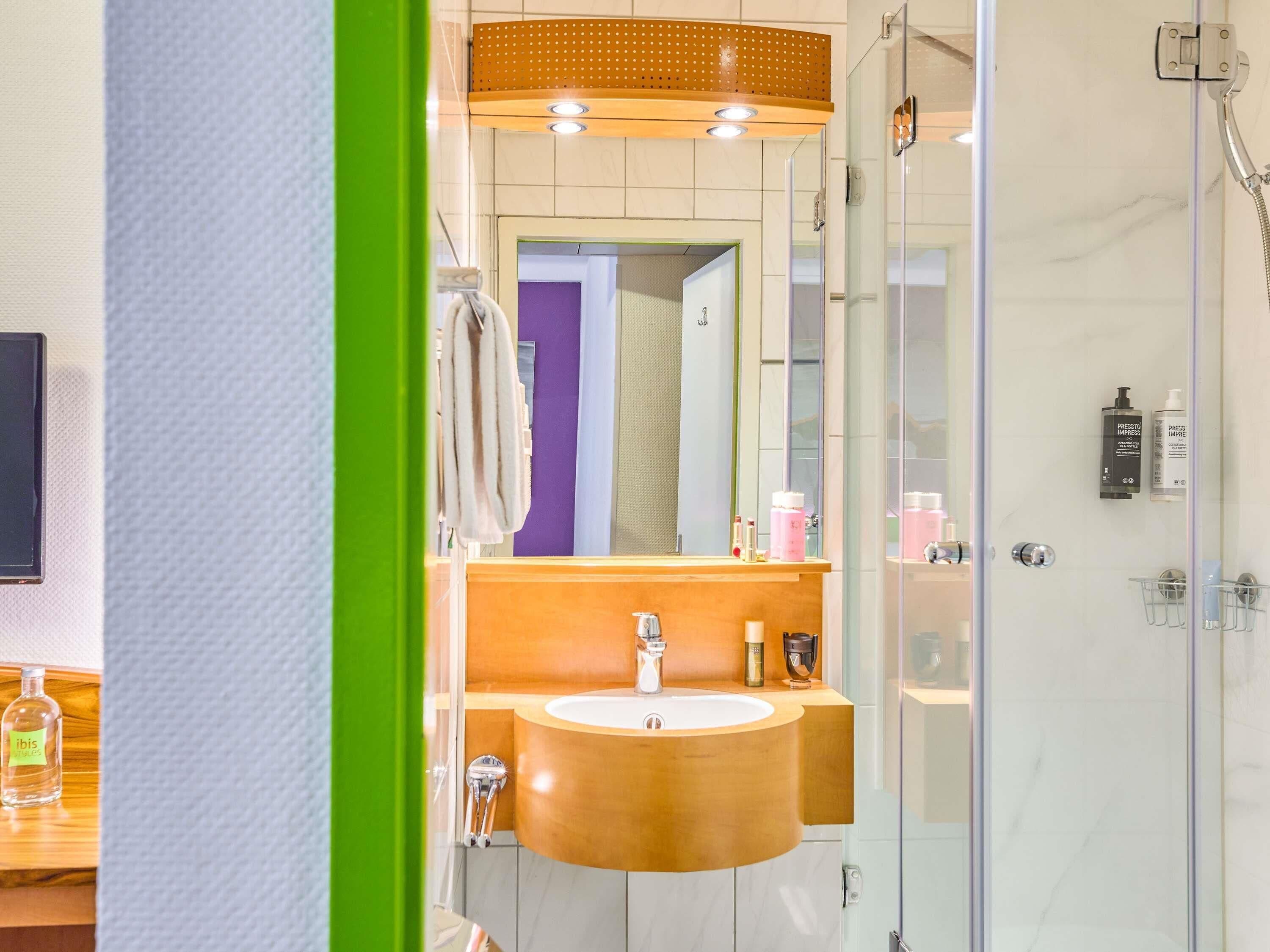 A modern bathroom with a wooden vanity, a glass shower enclosure, and a mirror above the sink.