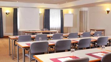 Un salón de conferencias con mesas, sillas, una pantalla de proyector y una pizarra.