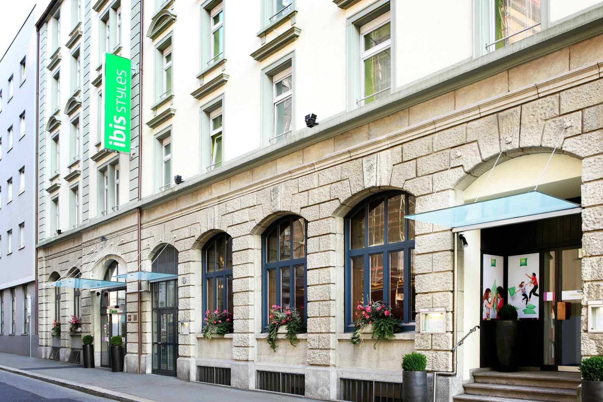 Un edificio histórico con fachada de piedra, ventanas en arco y un letrero verde que dice 'ibis styles'.