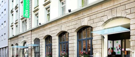 Un edificio histórico con fachada de piedra, ventanas en arco y un letrero verde que dice 'ibis styles'.
