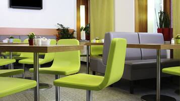 A modern dining area with green chairs, a grey sofa, and a flat-screen TV mounted on the wall.