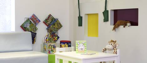 Una habitación infantil con un sofá blanco, una mesita con un juguete de jirafa y un taburete verde.