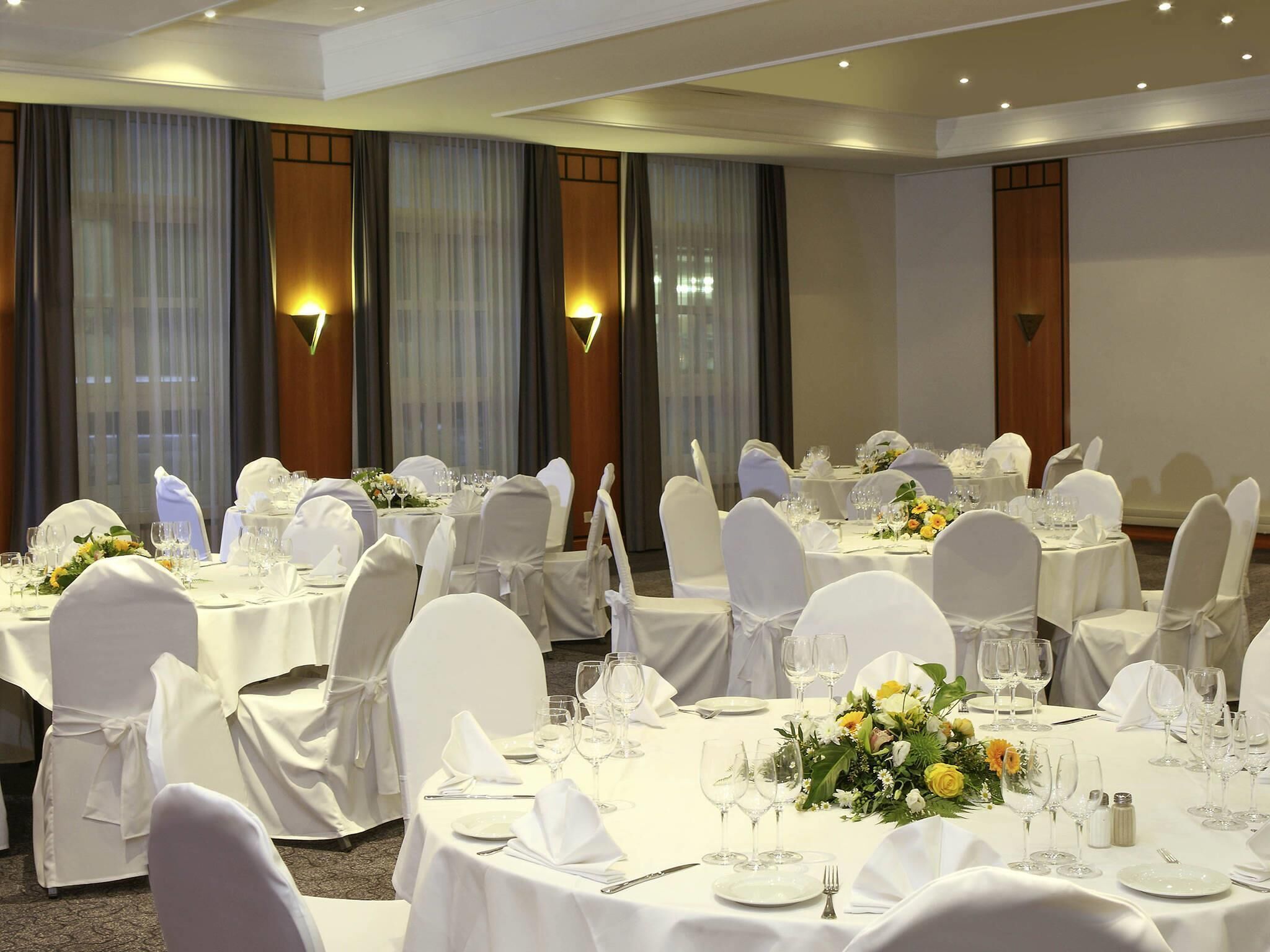 Un salón de banquetes con mesas redondas, manteles blancos y sillas con fundas blancas.