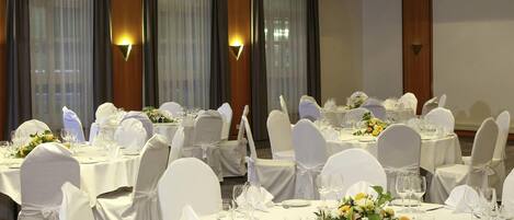 Un salón de banquetes con mesas redondas, manteles blancos y sillas con fundas blancas.