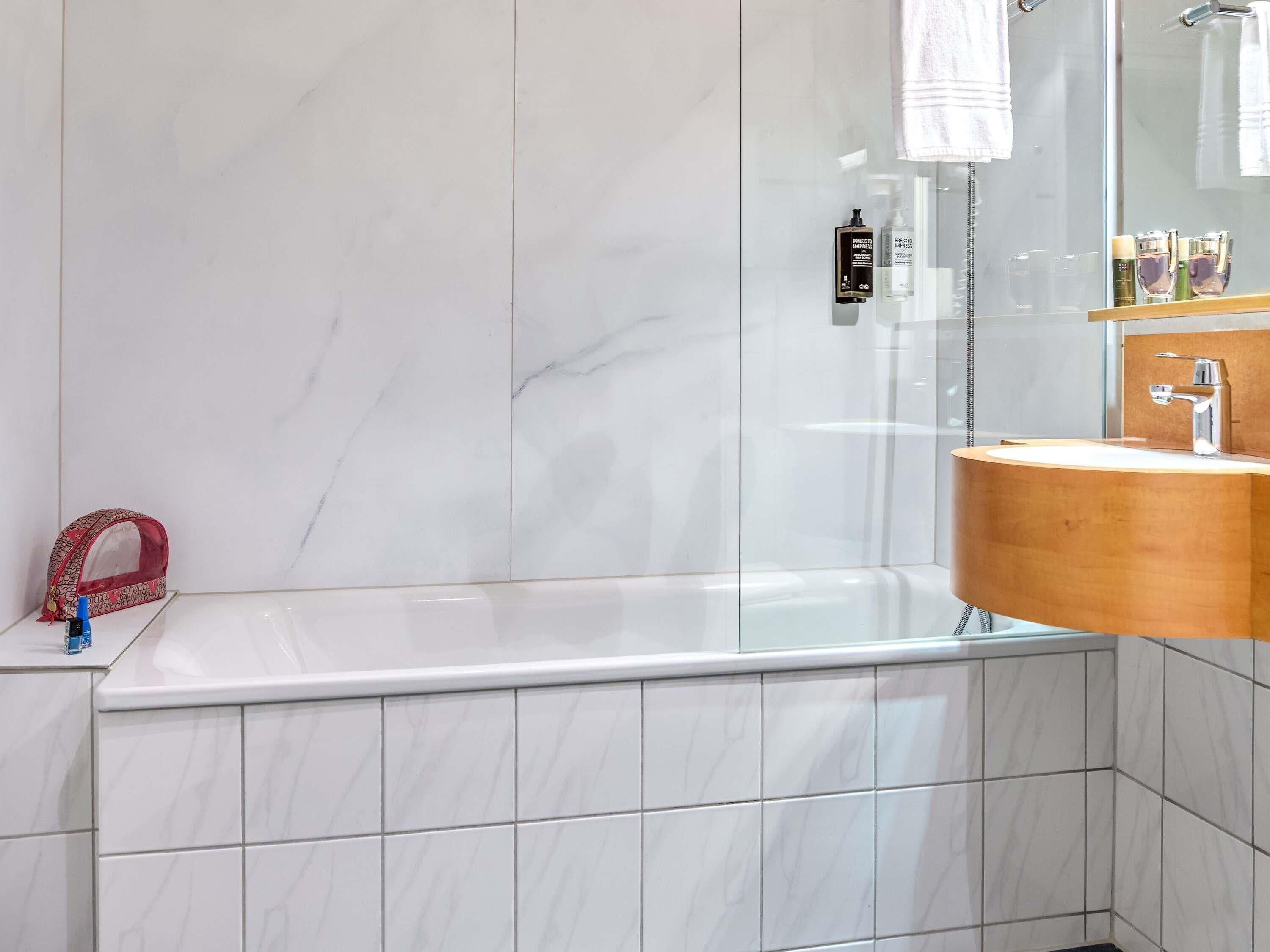 A bathroom with a marble wall, a wooden vanity, a bathtub, and a mirror.