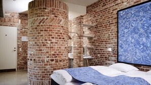A bedroom with a brick wall, a bed with white linens, a blue floral bedspread, and a large blue floral artwork on the wall. - Hindsgavl Slot (Middelfart)