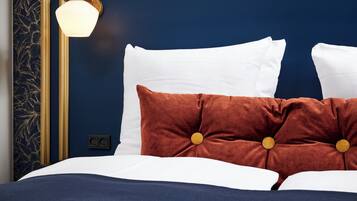 Una cama bien hecha con almohadas blancas y marrones, una pared azul oscuro y una lámpara de pared.