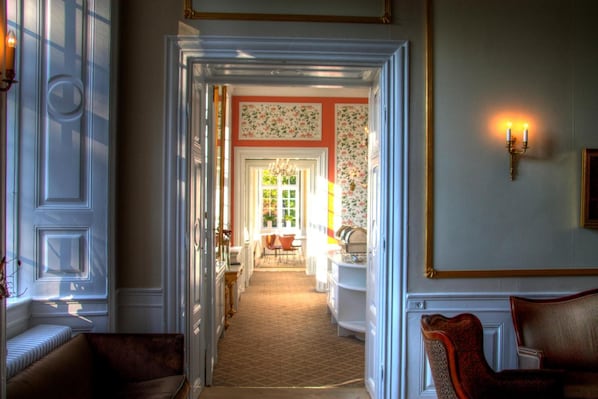 Un couloir doté d’un sol recouvert de moquette, un coin repas avec des chaises et une table, et un mur orné d’un papier peint à motifs floraux.