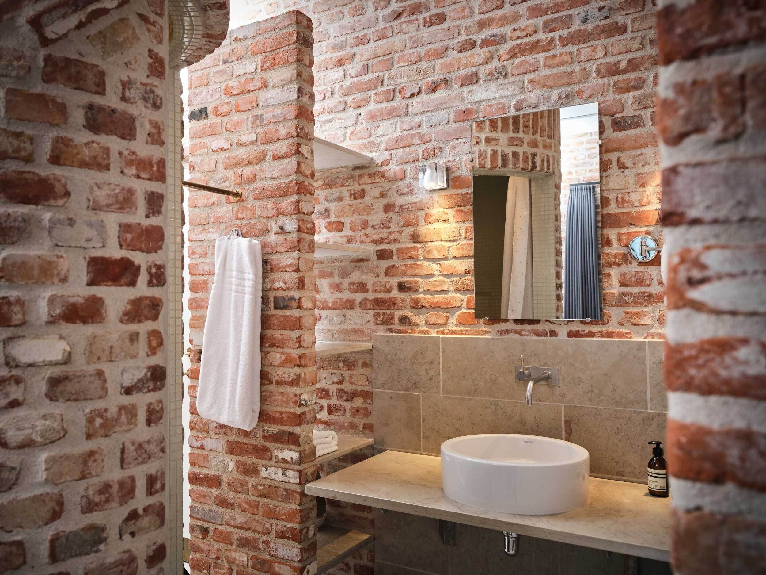 A bathroom with a brick wall, a white sink, and a towel hanging on the wall.