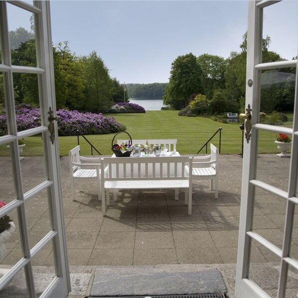 Une terrasse extérieure avec une table blanche dressée pour le repas, entourée de bancs blancs.