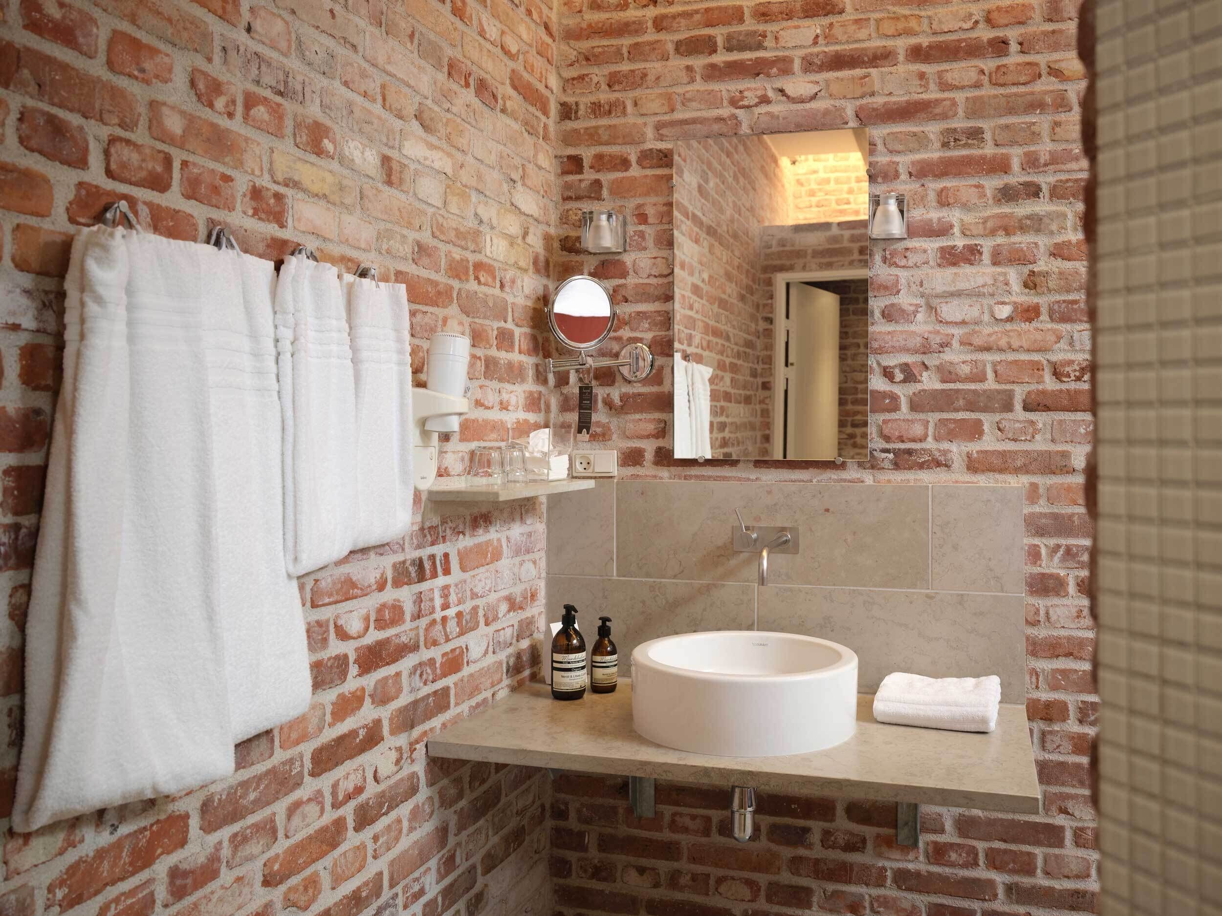 A bathroom with a brick wall, a round sink, and a mirror.