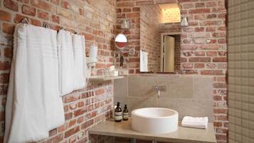 A bathroom with a brick wall, a round sink, and a mirror.