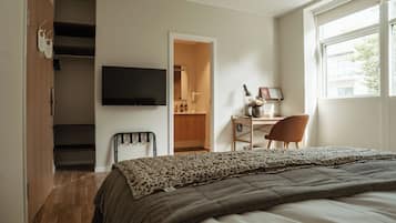 A bedroom with a bed, a desk, a chair, a TV, a wardrobe, and a window.
