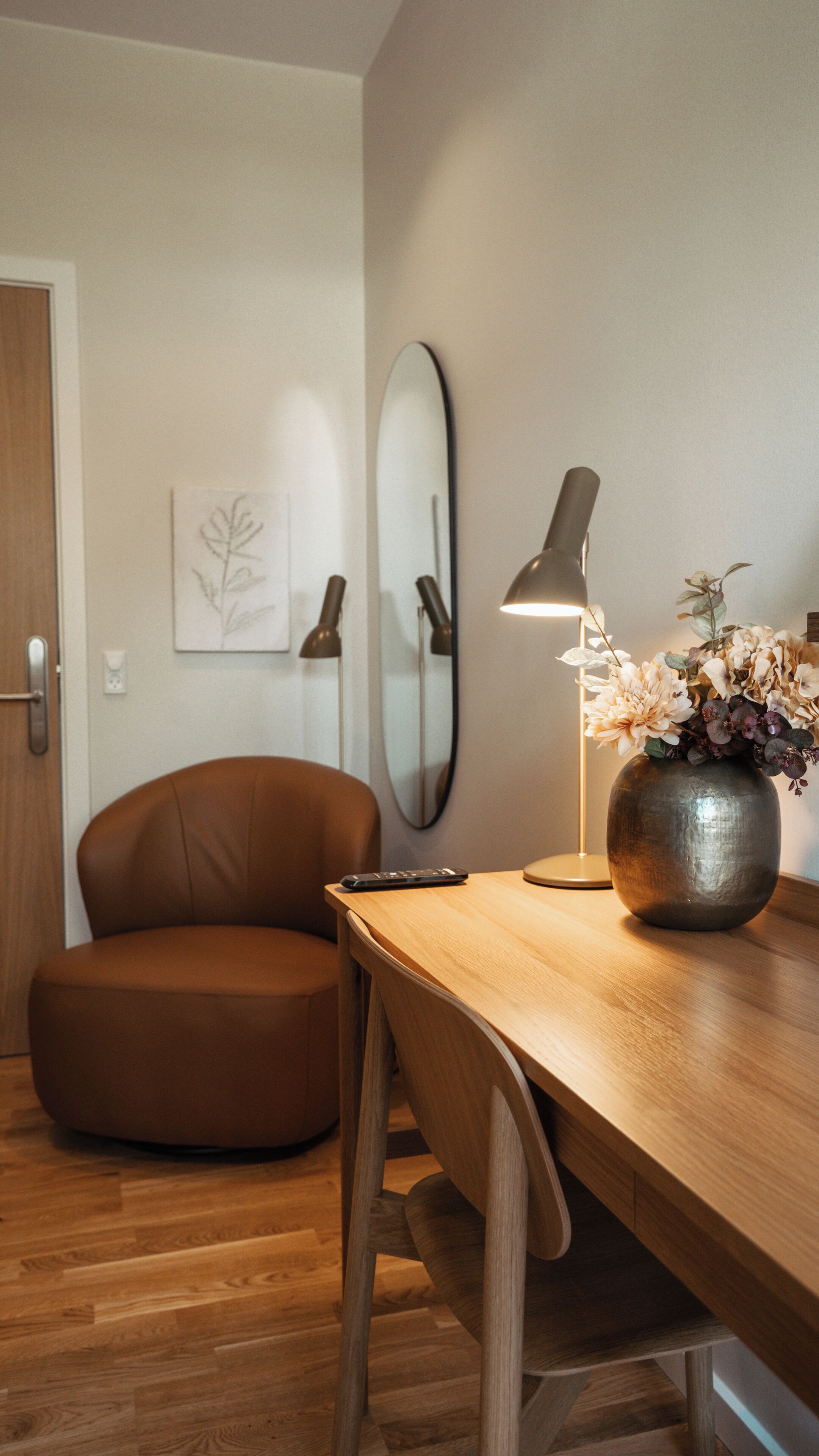 A modern room with a wooden desk, a brown leather chair, a lamp, and a vase with flowers.