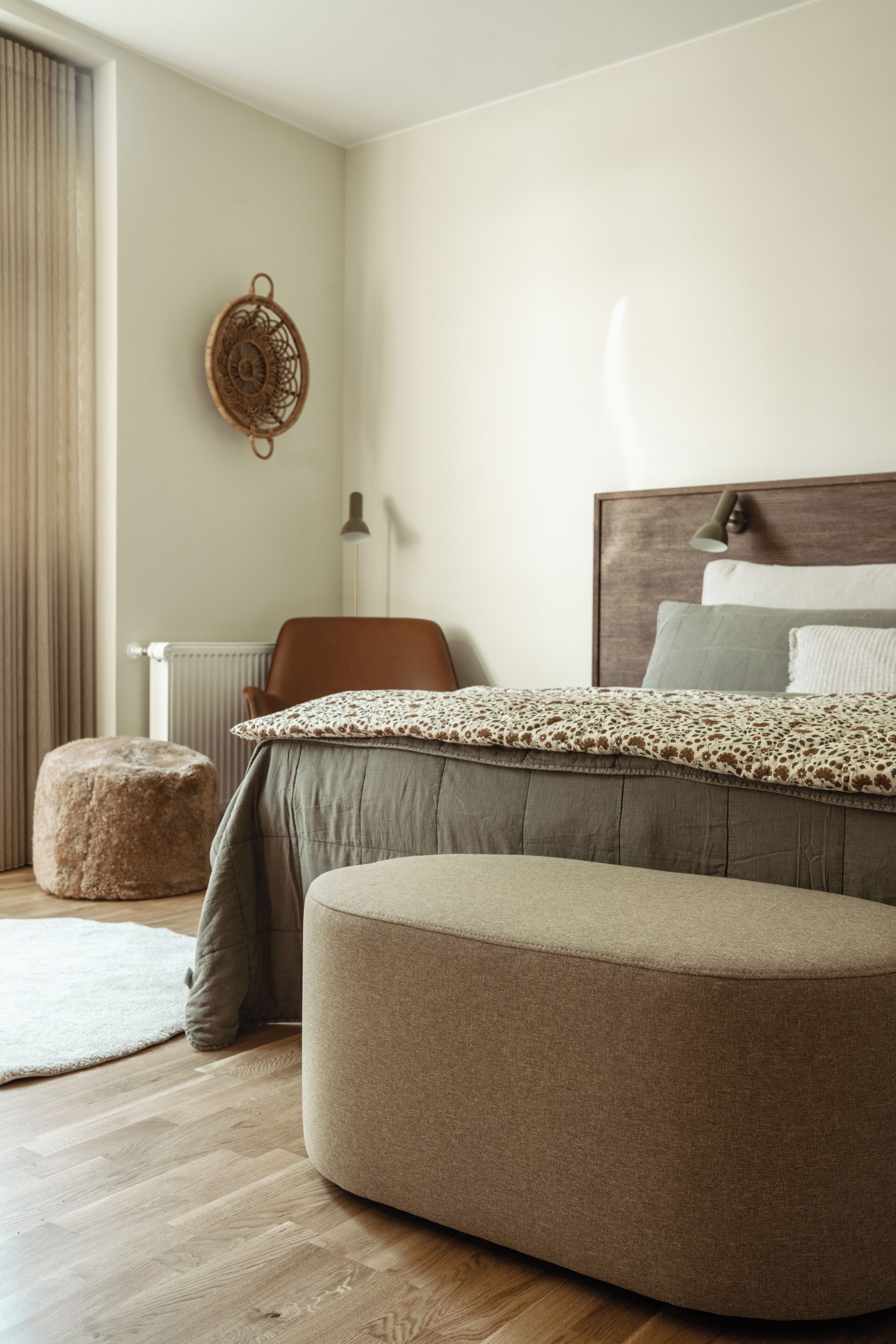 Un dormitorio moderno con una cama grande, un taburete redondo, una silla y un objeto decorativo en la pared.