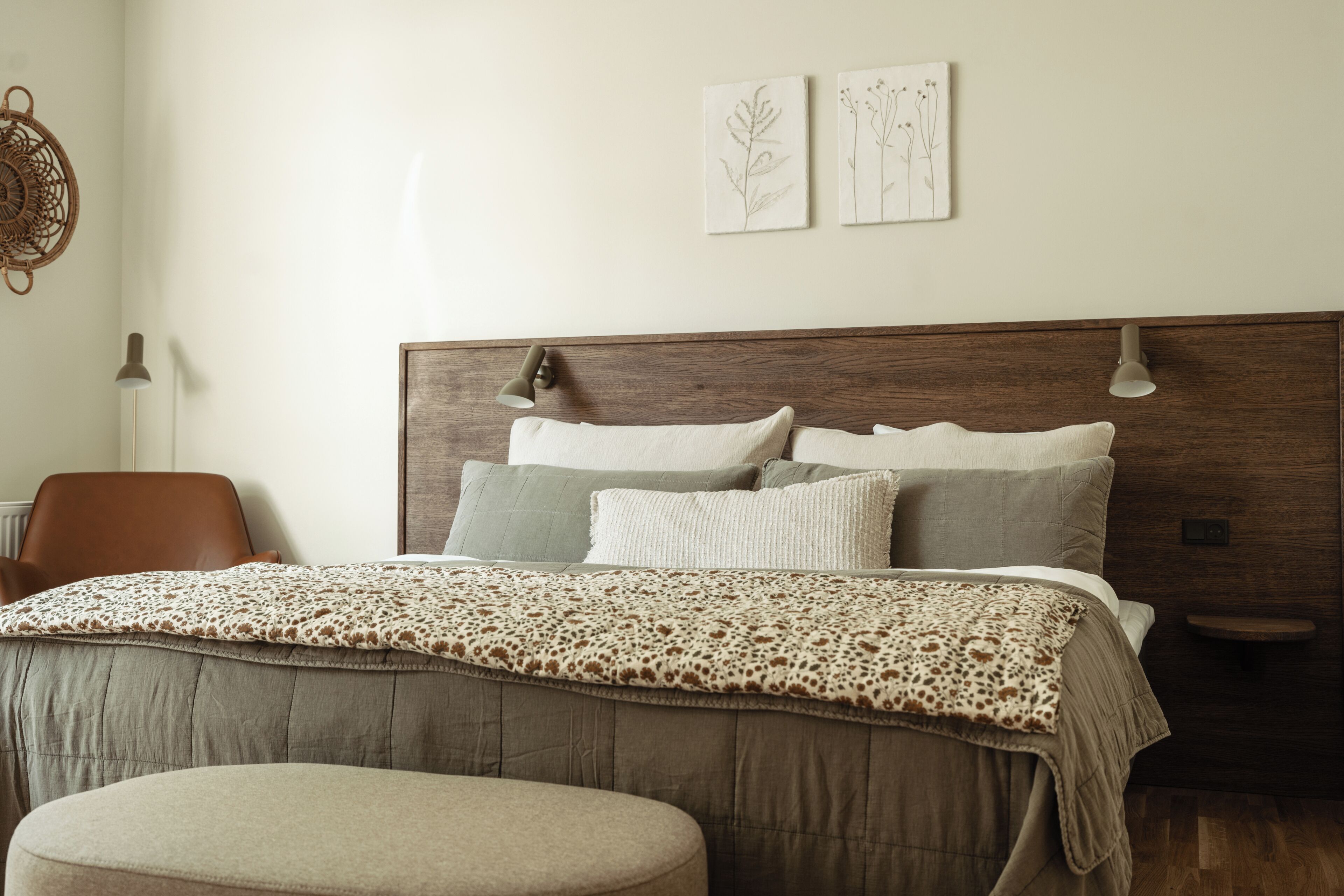 A bedroom with a wooden headboard, a bed with multiple pillows, a bedside table, a chair, and wall art.