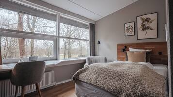 A bedroom with a large window, a bed, a chair, and two framed botanical prints on the wall.