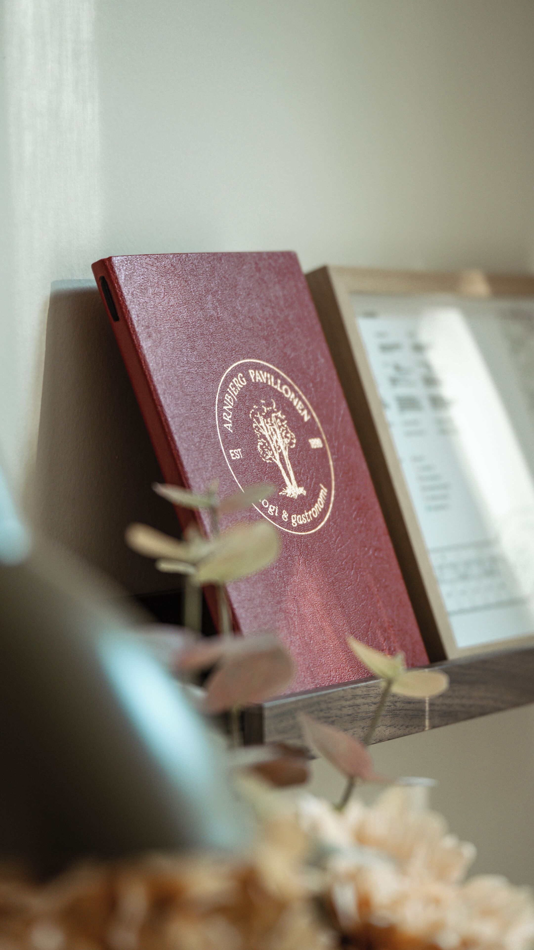 A red book with a gold emblem on a wooden surface, partially obscured by a blurred object.