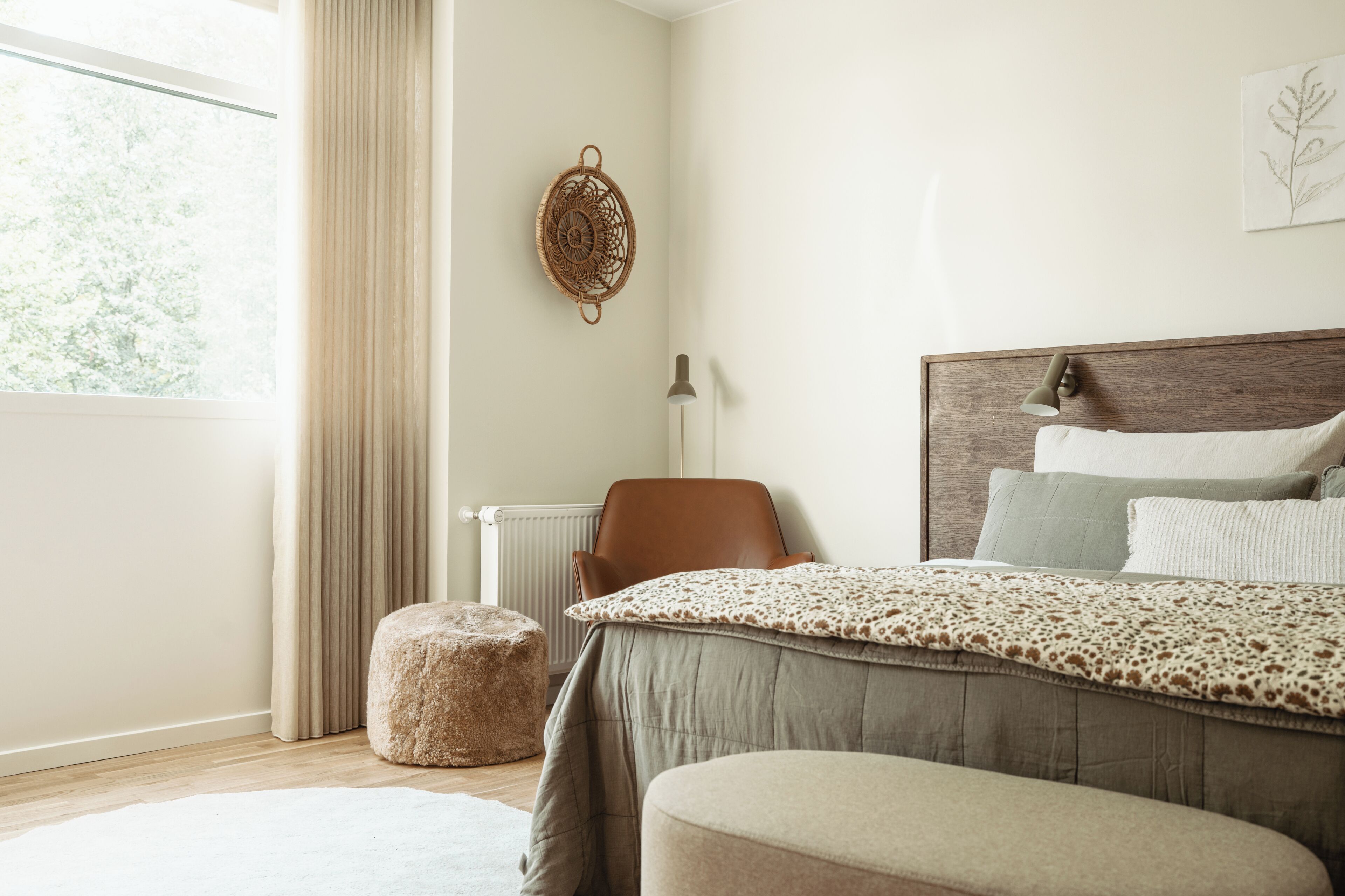 Ein Schlafzimmer mit einem Bett, einem Sessel, einem Heizkörper, einem Fenster mit Vorhängen und einer Wanddekoration.