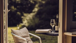 A view from inside a room to an outdoor patio area with a chair, a table, a glass of wine, and a bottle of wine. - Arnbjerg Pavillonen (Varde)