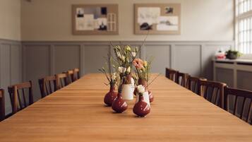 Una larga mesa de madera con arreglos florales en jarrones, sillas de madera y cuadros en la pared.