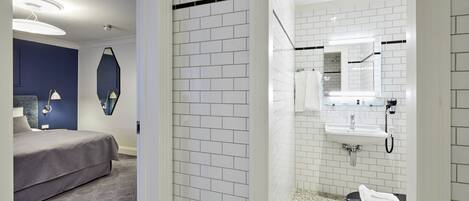 A modern hotel room with a bed, a bathroom with white tiles, a sink, and a mirror.