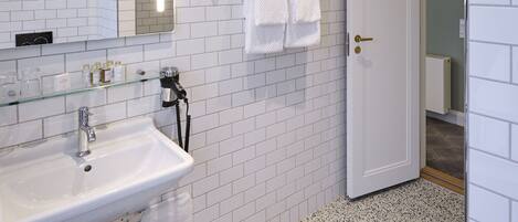 Un baño moderno con azulejos blancos tipo metro, cabina de ducha de vidrio, lavamanos blanco y un perchero para toallas.