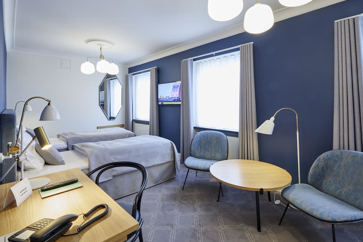A hotel room with two beds, a desk with a telephone, a chair, a small table, and a TV on the wall.