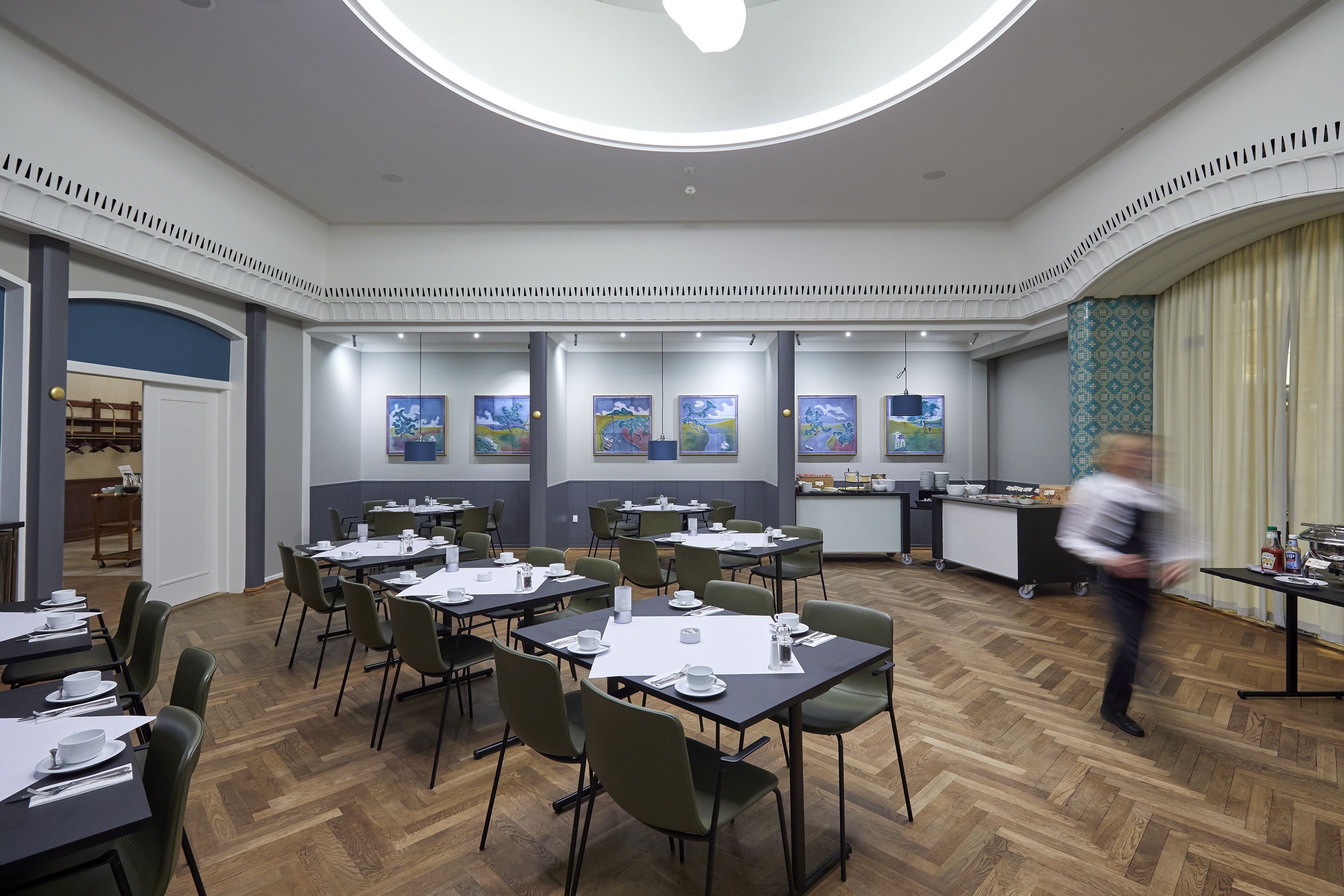 A modern dining area with multiple tables and chairs, a kitchen area, and artwork on the walls.