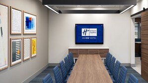 A conference room with a long table, blue chairs, framed artwork on the walls, and a Holiday Inn Express sign on the wall. - Holiday Inn Express and Suites Oklahoma City Northwest by IHG (Oklahoma City)