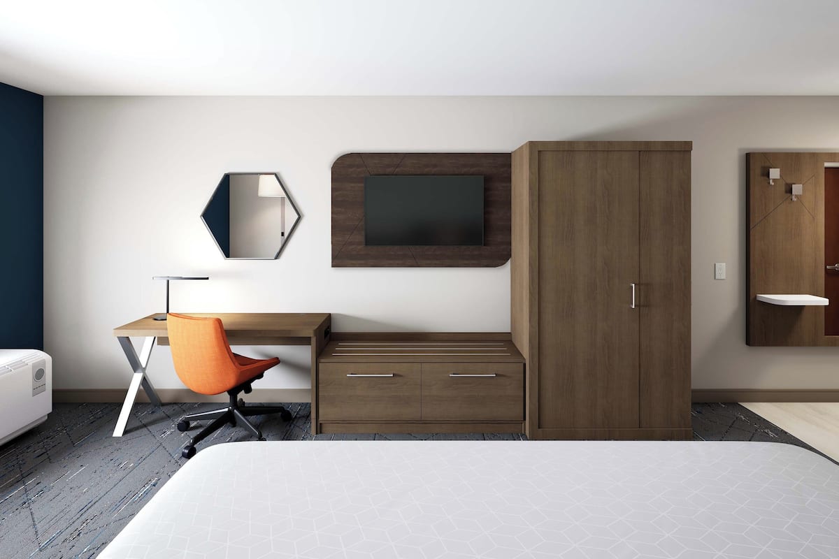 Une chambre d’hôtel moderne équipée d’un lit, d’un bureau avec une chaise, d’une armoire, d’une télévision et d’un miroir.