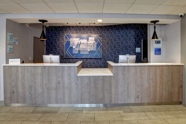 Ein Hotelrezeptionsschalter mit zwei Computerarbeitsplätzen, einer blauen Wand mit Muster und einem Holzboden.