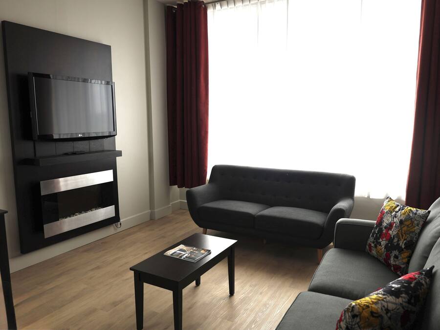 Una sala de estar moderna con un televisor de pantalla plana montado en una pared negra, un sofá gris con cojines de colores y una mesa de centro de madera.