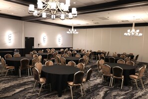 Un salón de conferencias con mesas redondas, sillas, candelabros y suelo alfombrado.