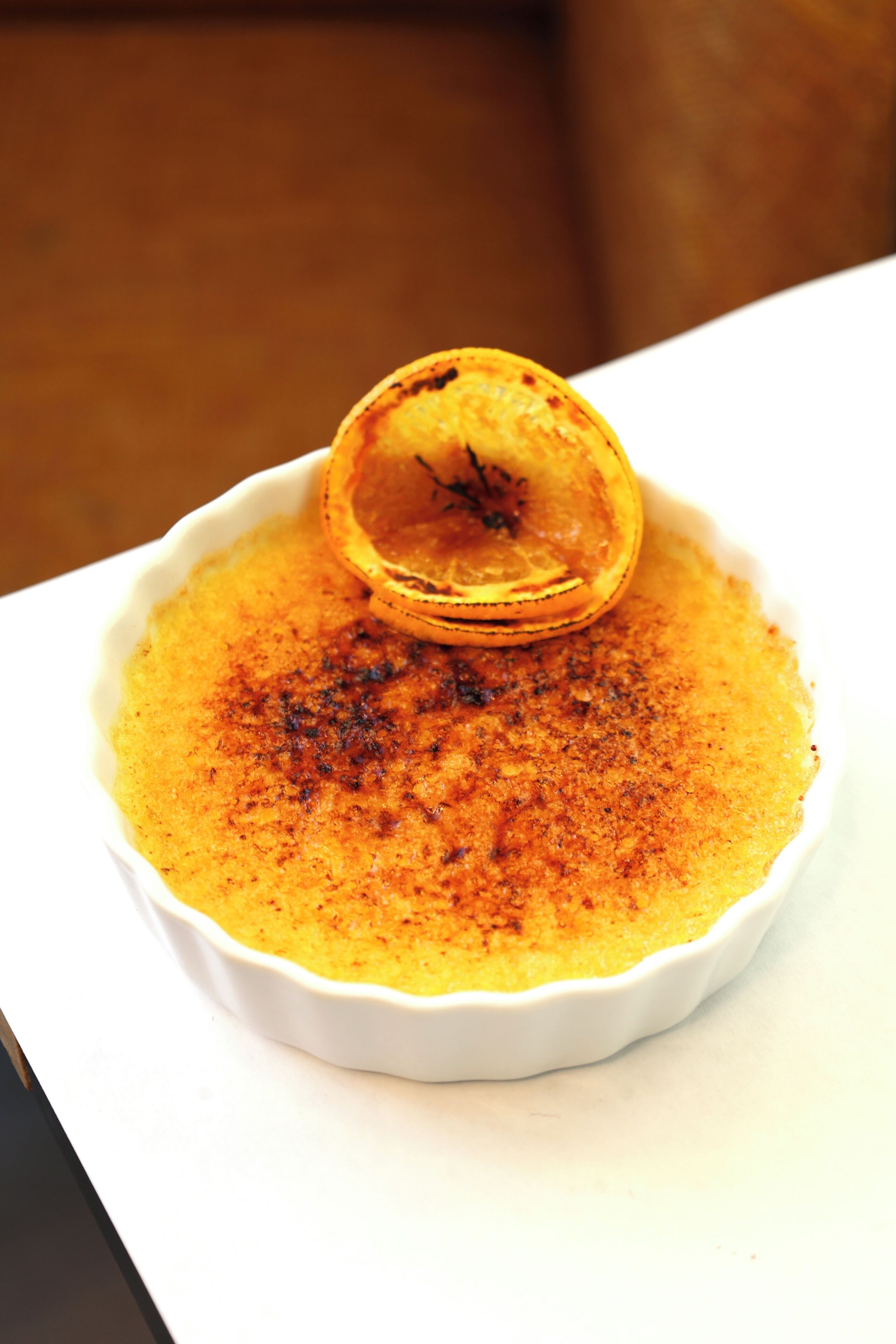 A white ceramic dish with a dessert, possibly crème brûlée, garnished with a slice of orange.