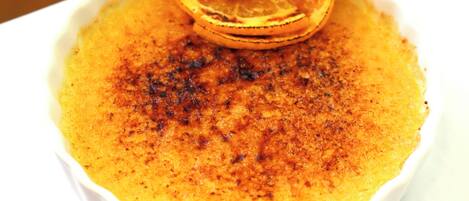 A white ceramic dish with a dessert, possibly crème brûlée, garnished with a slice of orange.