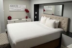 A neatly arranged bedroom with a large bed, a bedside table, a dresser, and a mirror on the wall.