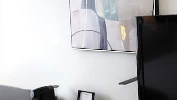 Habitación de hotel moderna con escritorio, televisor de pantalla plana, un cuadro enmarcado y cafetera.