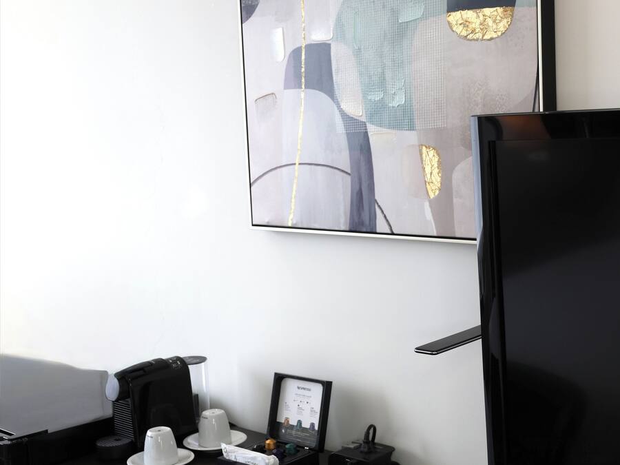 Habitación de hotel moderna con escritorio, televisor de pantalla plana, un cuadro enmarcado y cafetera.