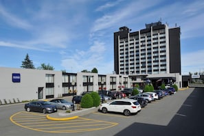 A parking lot with cars, a building with a sign 'Transbridge,' and a tall building in the background.