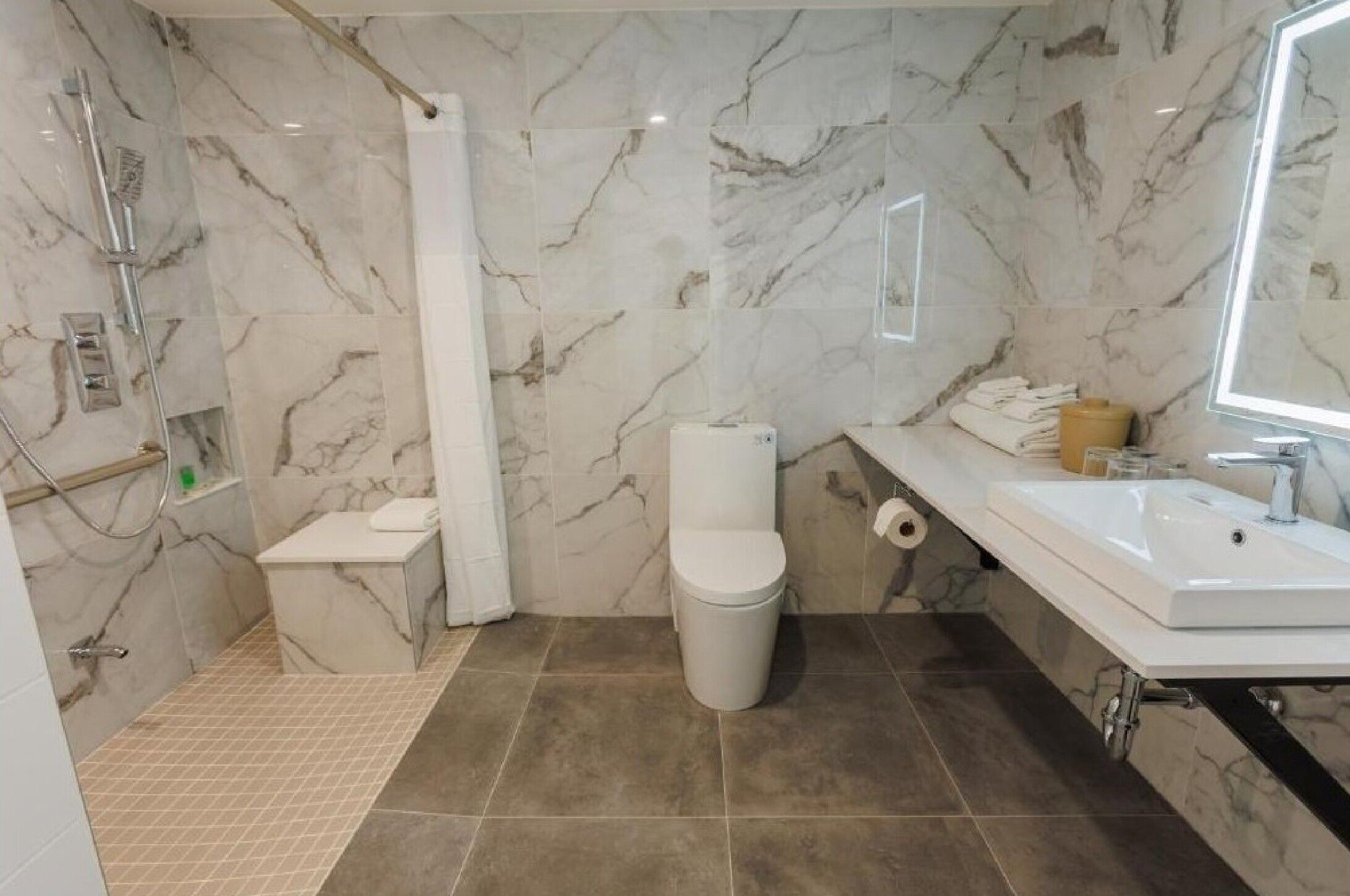 A bathroom with a shower, toilet, sink, and marble walls.